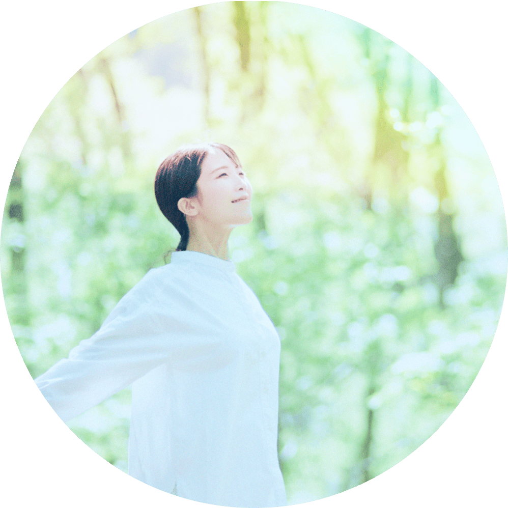 木漏れ日が広がる爽やかな空間で、白いトップス姿の女性が心地よさそうに空を見上げる様子